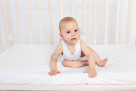 个月大的男婴穿着白色衣服坐在儿童房的婴儿床里图片