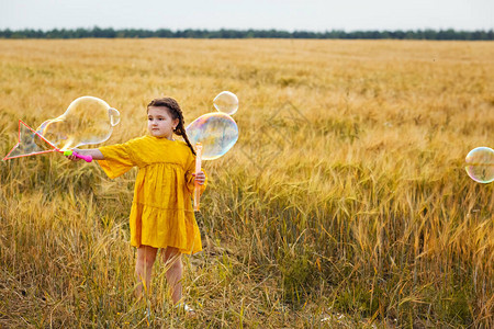 一个穿黄色裙子的女孩正在小麦田里玩耍吹图片