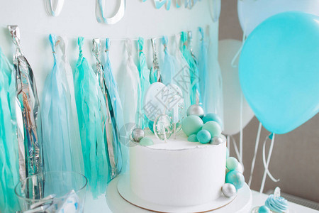 庆祝一岁男婴的节日装饰架子上的白蛋糕纸杯蛋糕蓝色球和金属丝题字图片