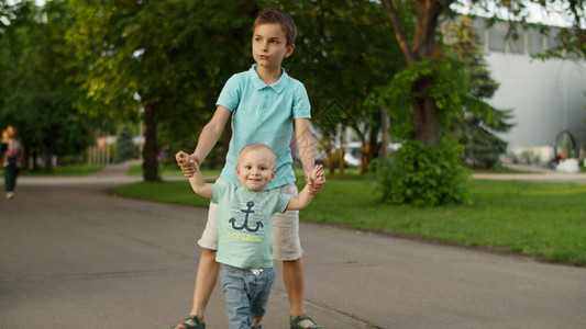 两个男孩在慢动作中去绿色公园轻松的母亲带着三个孩子在户外散步哥带着初图片