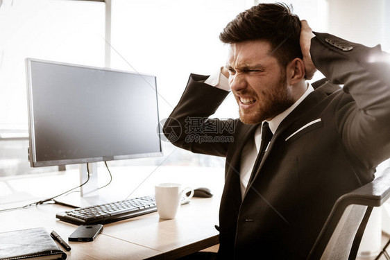 商业危机概念情绪化的年轻商人在工作坐在办公桌前的忧心忡的经理用手撕扯他的头发在室内穿西装的忙碌男人表图片