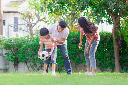 快乐的家庭父亲母亲和儿子在家里的院子里一起踢足球作为活动父母和孩子之间的关系或纽带享受周末的图片