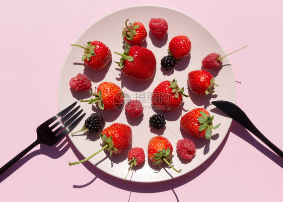 粉红色背景上粉红色陶瓷盘中的新鲜浆果草莓覆盆子黑莓素食或水果饮食图片