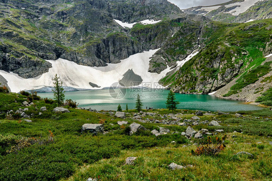 高山上美丽的绿松石湖山坡上的冰川供给湖水前景有大石头的山景和被群图片