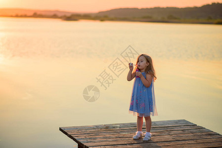 一个小女孩在湖边的码头上吹泡图片