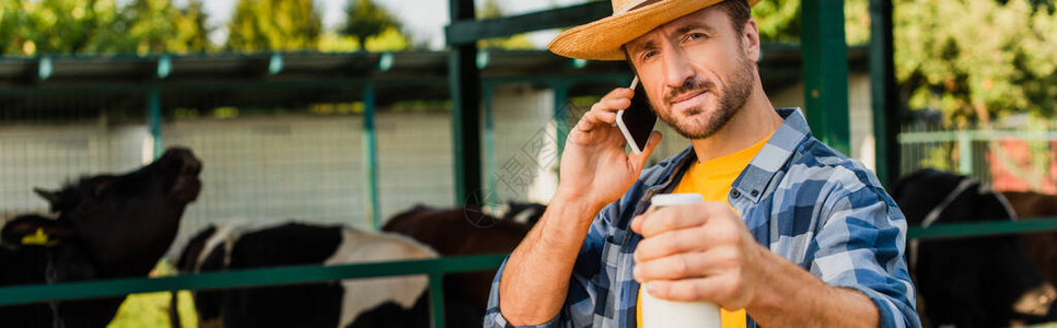 农民用草帽和格衬衫在移动电话上交谈时持有一瓶牛奶的图片
