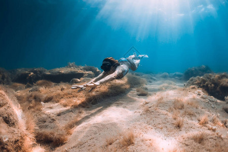 自由潜水的女人有鳍在深海和阳光下滑图片