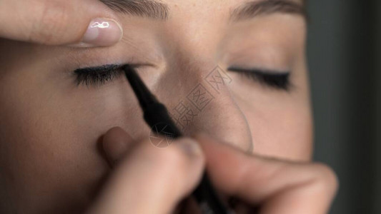 化妆艺术家在美容工作室为年轻女做专业化妝艺术家将黑眼线应用到眼皮图片