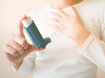 穿着白色T恤的年轻女使用蓝色哮喘吸入器缓解哮喘发作医药产品用于预防和治疗由哮喘或慢阻塞肺病引起的喘息和呼背景图片