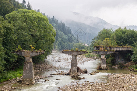 一座倒塌的桥梁矗立在山区河流上图片