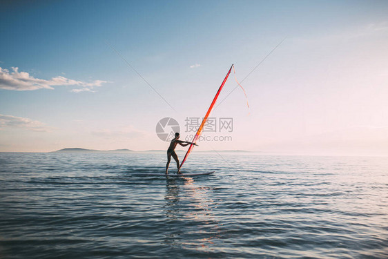 年轻人隆起风帆冲浪板帆冲浪者在日落海上风冲浪板上保持平衡风帆冲浪图片