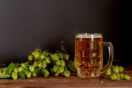 木制背景上的一杯新鲜啤酒和绿色啤酒花图片