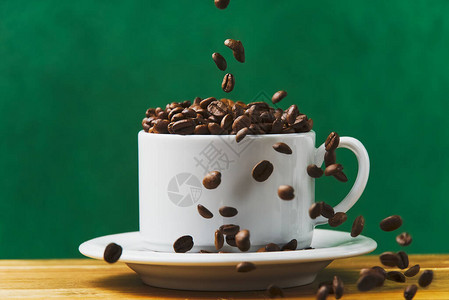 国际咖啡日概念特写白色咖啡杯装满咖啡豆咖啡豆落入白色杯子分图片