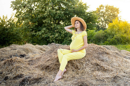一名身着黑衣服和帽子的孕妇夏天坐在草背景图片