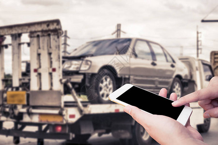 使用移动智能手机进行紧急路边应急交通服务的手与交通事故背景后拖车吊图片
