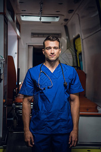 穿着蓝色制服的年轻医生站在一辆救护车前看镜头图片