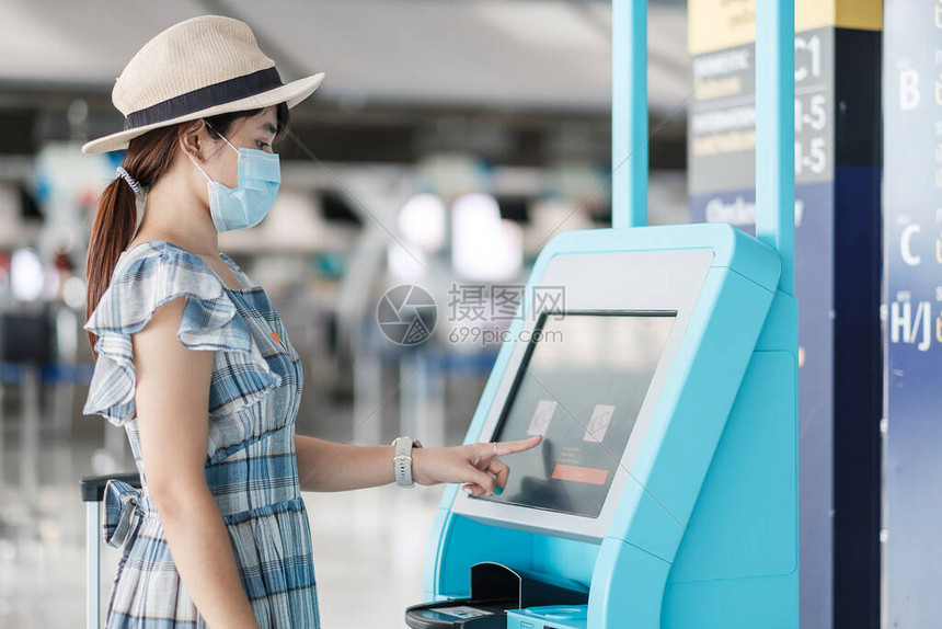 戴着医用口罩并在机场航站楼使用自助值机领取登机牌的亚洲女旅客准备旅行COVID19下的新常图片