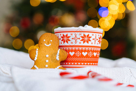 书与咖啡圣诞明信片与姜饼人红色杯子与圣诞装饰品从圣诞树和红色条纹节日糖果的光散景白色针织上带棉花糖的圣背景