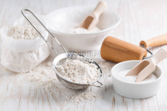 在白色木桌上拼写面粉糖和烘焙原料和厨房用具图片