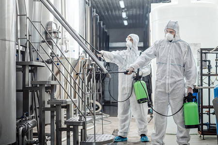 身穿防护服和面罩的男子在工厂空间用化学喷雾袋进行防腐图片