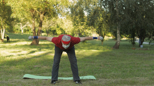 白种老人独自在公园里用哑铃做健身运动老年人锻炼运动的老祖父养老金领取图片