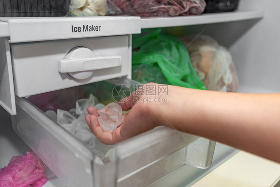 女孩从冰箱的制冰机里取冰块来冷却图片