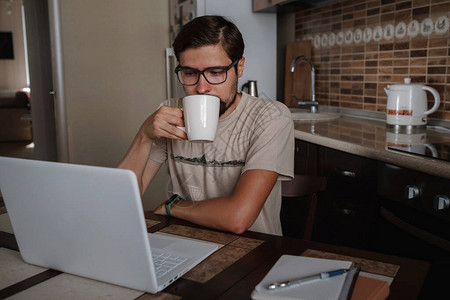 坐在桌边喝咖啡的年轻企业家在笔记本电脑上思考问题的解决方案图片