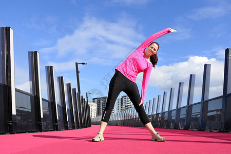 年轻女30岁在新西兰奥克兰的一条明亮粉红色自行车道上跑前先热身图片