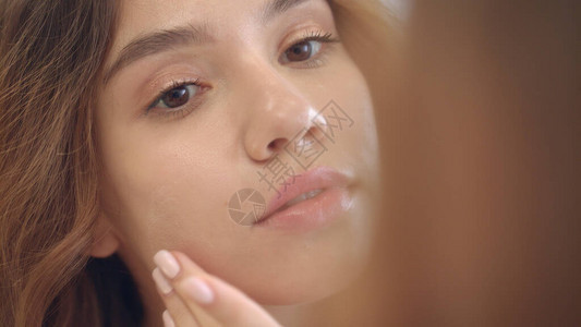 微笑的女人在浴室镜子里的脸上涂抹保湿霜图片