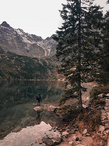 站在一块被高山和树木环绕的清澈湛蓝绿色湖泊中间的大石头上图片