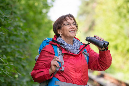 一个在森林里戴双筒望远镜的年长妇女的肖像图片