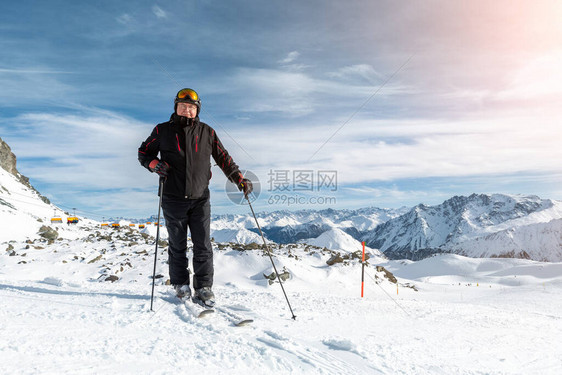 身着滑雪头盔护目镜和黑色西装的活跃资深老者站在山峰上享受冬季极限运动活令人惊叹的全景山图片