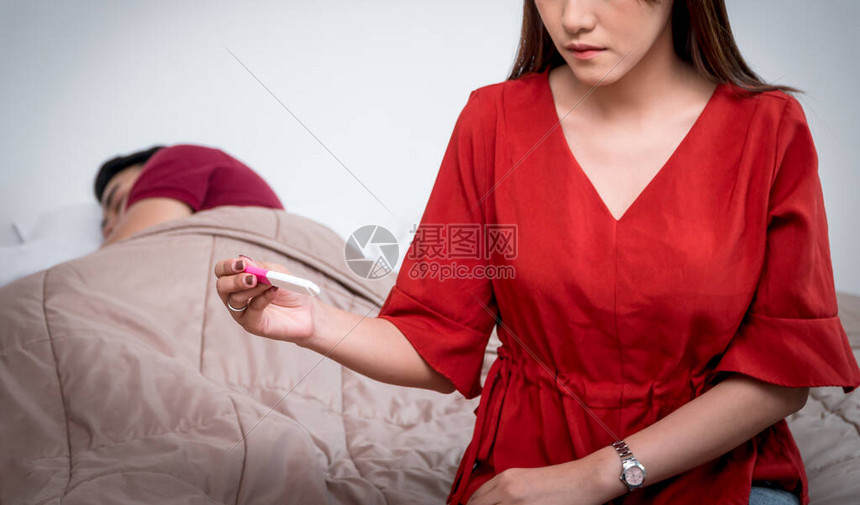 不开心的亚洲女人拿着和看妊娠试验图片
