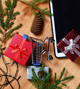 红色礼品盒蝴蝶结平板电脑圣诞树枝灯木制背景圣诞节和新年礼物的概念平图片