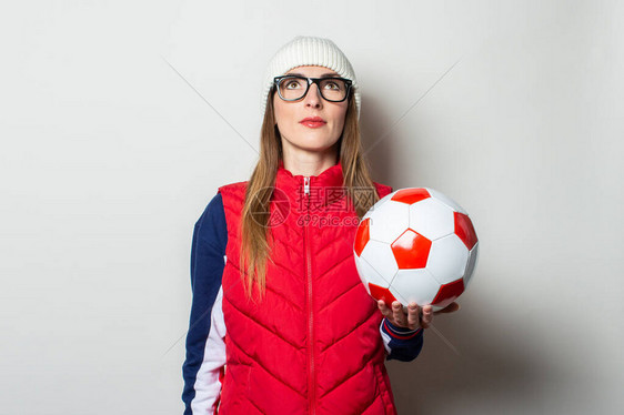 戴红背心戴帽子和戴眼镜的年轻女子拿着足球图片