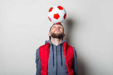 穿着帽子连帽和背心的年轻人头顶上带着一个足球图片