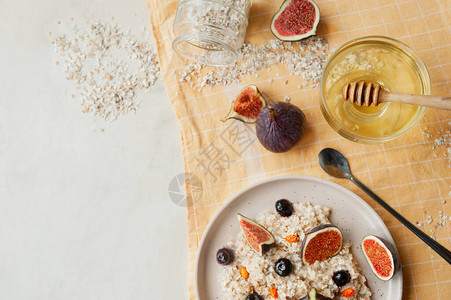 健康维生素早餐燕麦粥蓝莓新鲜无花果和黄棉餐巾蜂棒和长勺子上的海角图片
