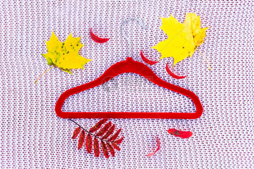 一个衣架躺在针织背景上的秋天五颜六色的树叶叶和红色衣架躺在针织毯子上从上面查看图片