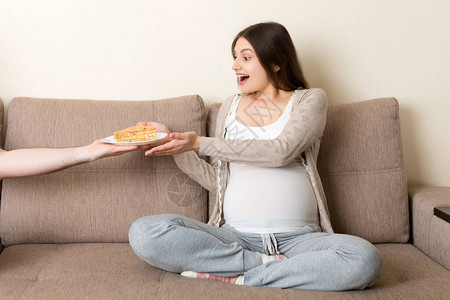 丈夫在家里的沙发上给怀孕的妻子一块蛋糕未来的父图片