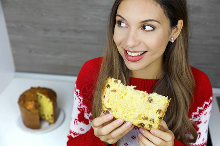 美丽的年轻女子在圣诞节日吃一片帕尼顿饼图片