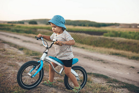 带着自行车和帽子的快乐男孩在一个夏天晚上在田里散步试图片
