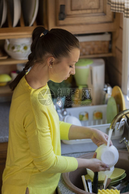 年轻漂亮的女家庭主妇在打扫厨房时洗碗图片