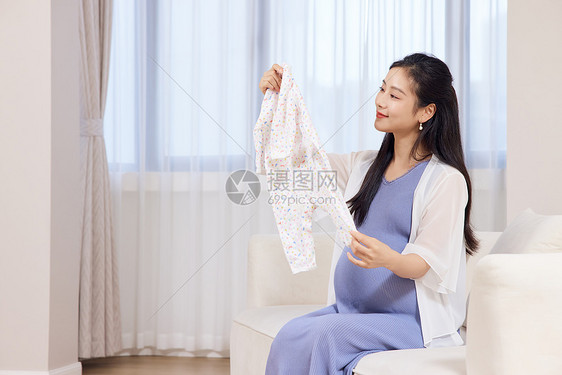 年轻居家孕妇手拿婴儿衣服图片