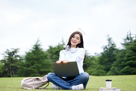 长发美女坐在草坪上电脑学习的女学生背景