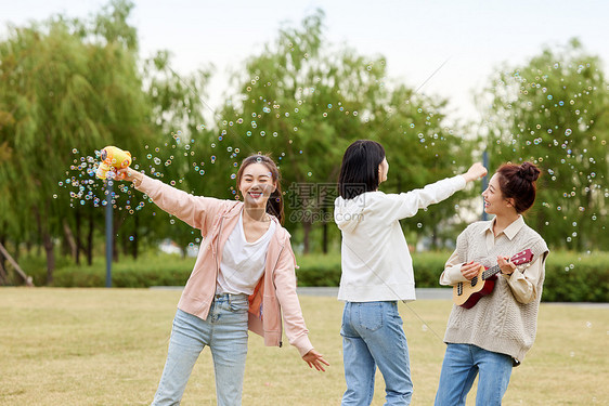 户外草坪玩泡泡机的女性闺蜜图片