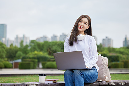 户外使用笔记本电脑的年轻美女大学生图片