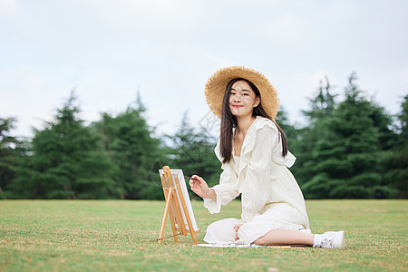 坐在草坪上绘画的青年女性图片