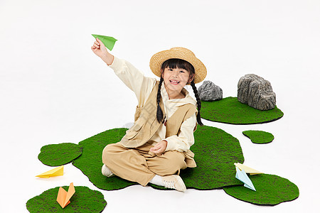 坐在草地上玩纸飞机的小女孩图片
