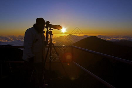 一位摄影师在Maui岛Haleakala火山顶端的戏剧日出前被围绕背景图片