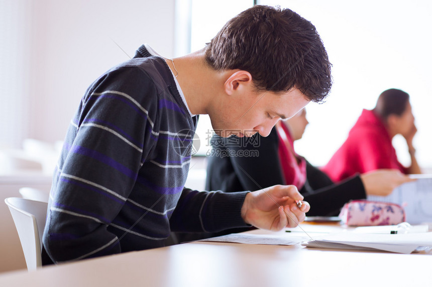 年轻英俊的男大学生上课时坐在满是学生的教室里高清图片下载-正版图片507011029-摄图网